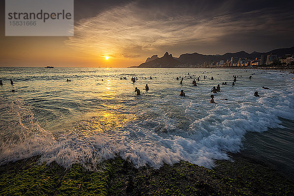 Badegäste am Strand von Ipanema Beach mit Wellenschlag bei Sonnenuntergang