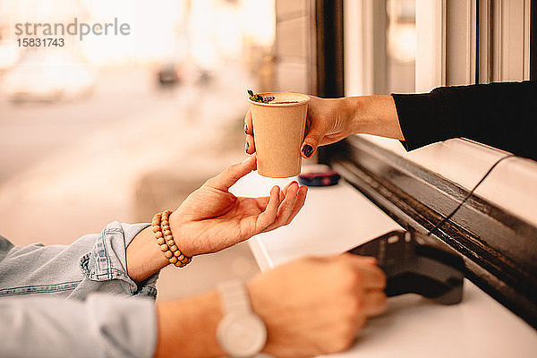 Weiblicher Barista gibt dem Kunden Kaffee  während er bezahlt