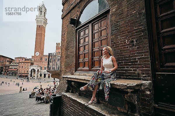 Weibliche Touristin sitzt auf Bank am alten Gebäude