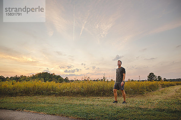 Ein stolzer Mann steht bei Sonnenuntergang am Rand eines goldenen Feldes vor blauem Himmel
