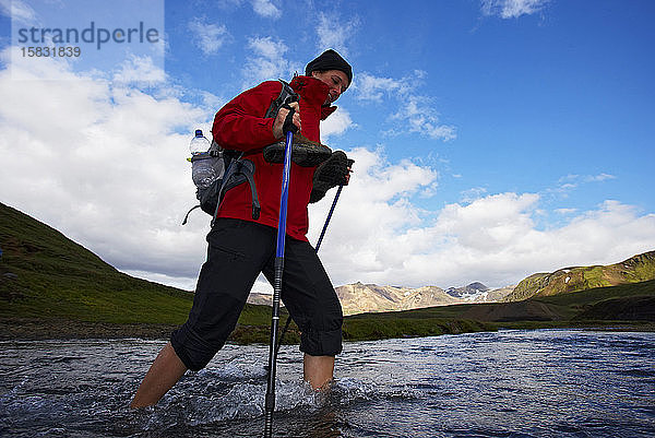 junge Frau überquert Fluss auf dem Laugavegur-Wanderweg