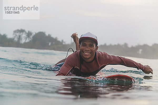 Porträt eines glücklichen Mannes  der auf einem Surfbrett auf dem Meer liegt