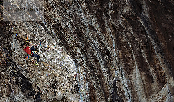 Kletterer  der eine harte Sportkletterroute in einer Höhle schickt.