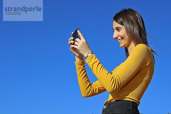 Schönes gelb gekleidetes Mädchen beim Fotografieren mit dem Telefon