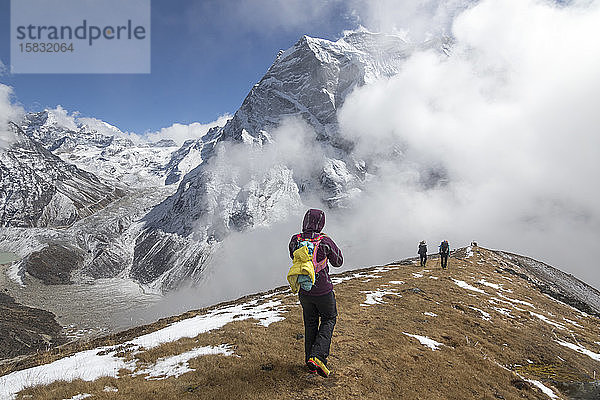 Eine Frau steigt einen sanften Grat in den Nebel hinab  Himalaya-Gipfel im Rücken
