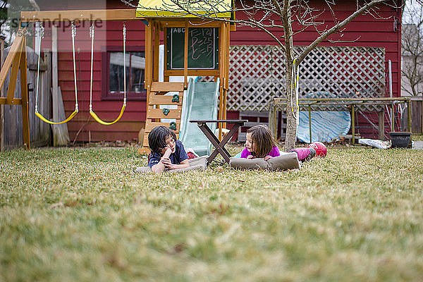 Zwei glückliche Kinder liegen auf Matten in ihrem Hof und unterhalten sich miteinander