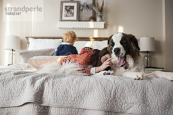 Kinder liegen mit großem Hund auf dem Bett  während Mädchen versucht  die Zunge des Hundes zu berühren