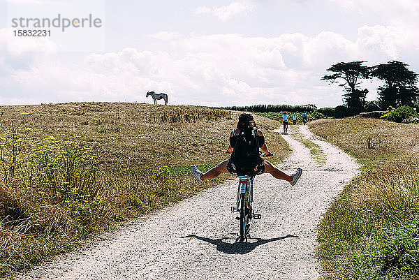 Hübsche junge Frau fährt Fahrrad mit offenen Beinen auf einer Landstraße