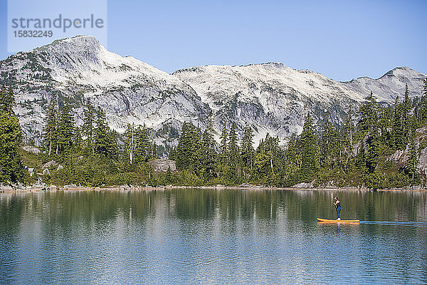 Seitenansicht einer aktiven Frau beim Paddelbootfahren auf einem Bergsee.