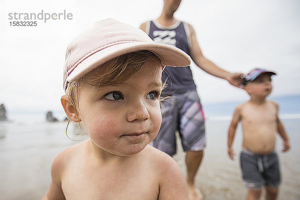Porträt eines süßen einjährigen Mädchens am Strand mit Bruder und Papa.