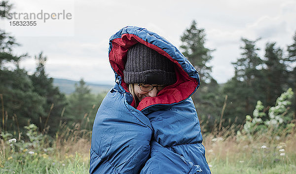 Porträt einer in einen Schlafsack gehüllten Frau  die wild im Freien zeltet