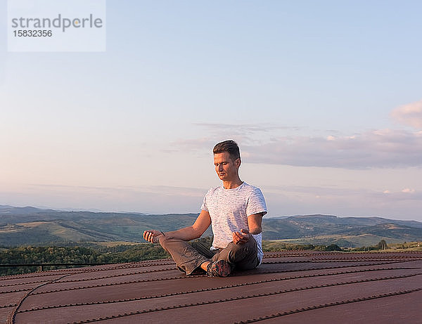 Erwachsener Mann meditiert auf der Terrasse in der Hitze der Umgebung s