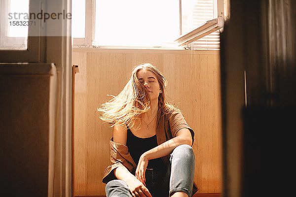 Teenager-Mädchen  das im Sommer auf dem Balkon auf dem Boden sitzend mit den Haaren wackelt