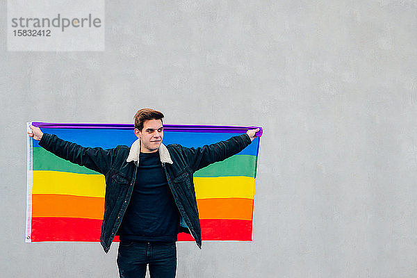 Junger Mann mit der Gay-Pride-Flagge auf grauem Hintergrund