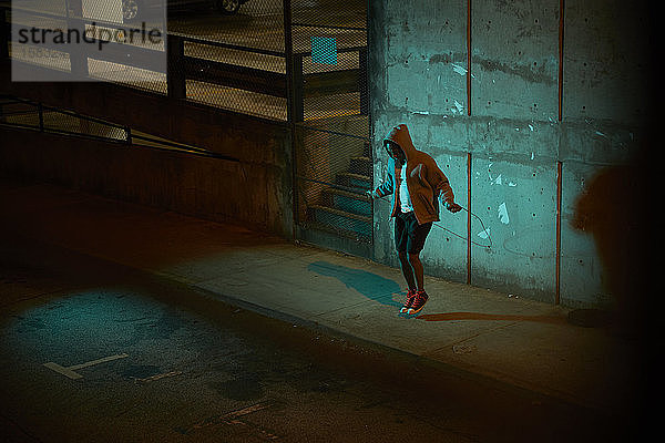 Afroamerikanischer Mann mit Kapuzenpulli trägt nachts Springseil