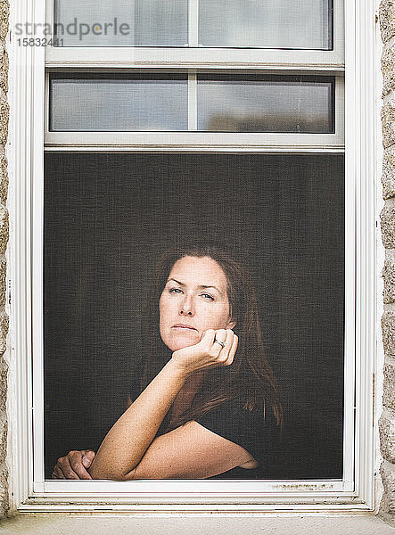 Frau schaut aus dem offenen Fenster  das Kinn auf der Hand ruhend.
