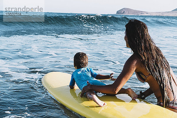 Junge Mutter und Sohn paddeln auf einem Surfbrett auf See
