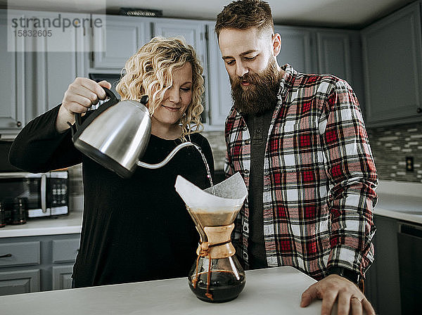 Lächelndes junges Paar kocht morgens Kaffee in ihrer Küche