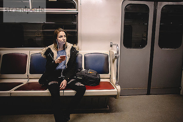 Junge Frau  die in der U-Bahn mit einem Smartphone Musik hört