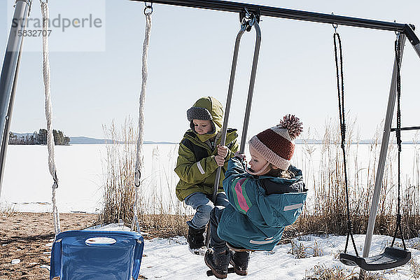 Kinder  die in Schweden gemeinsam auf einer Doppelschaukel am Meer spielen