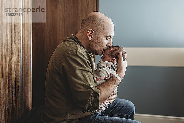 Seitenansicht eines glücklichen Vaters  der ein Neugeborenes im Krankenhaus küsst