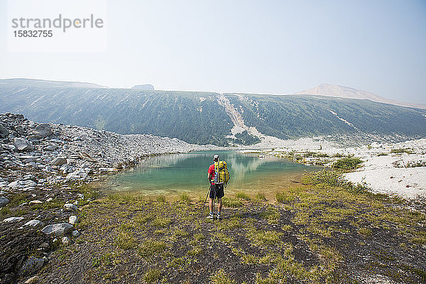 Rückansicht des Rucksacktouristen mit Blick auf den alpinen Bergsee.