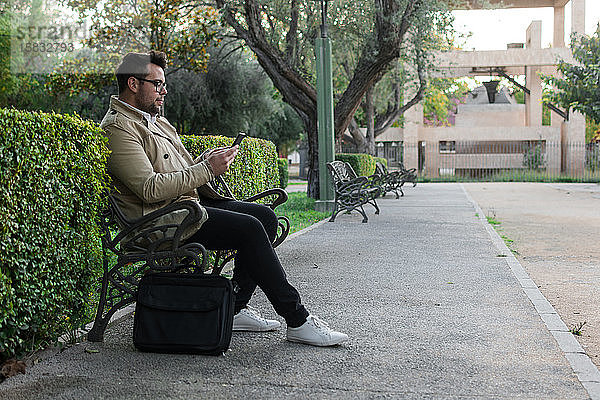 Geschäftsmann sieht sein Smartphone auf einer Parkbank