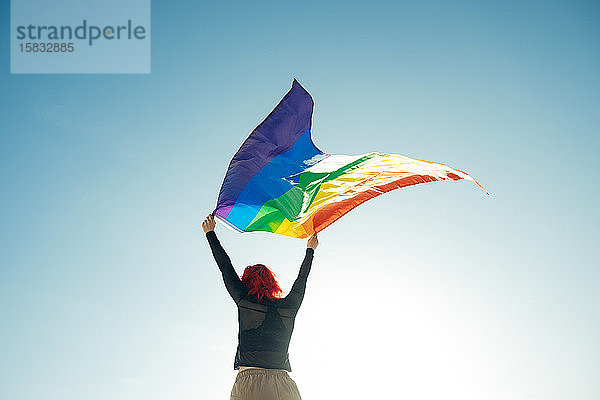 Frau hält die schwule Regenbogenfahne auf blauem Himmelshintergrund. Glück  Freiheit und Liebeskonzept für gleichgeschlechtliche Paare.