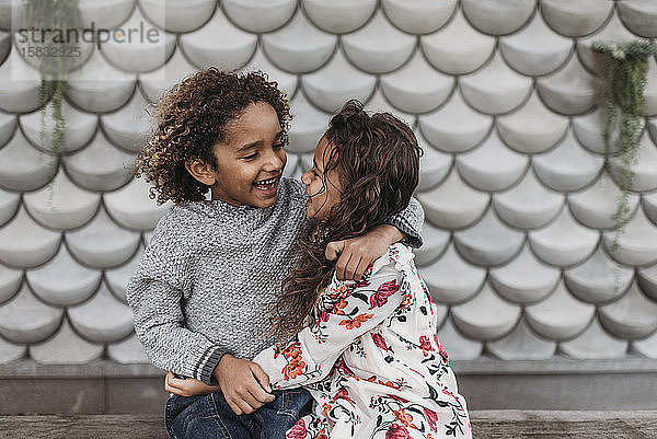 Süße Geschwister lächeln und lachen einander an  während sie sich draußen umarmen