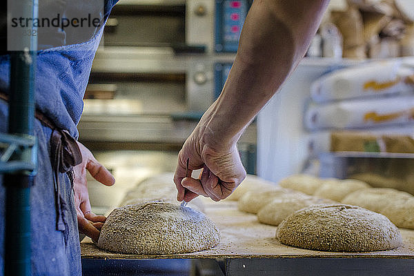 Nahaufnahme eines Bäckers  der einen Brotteig mit Samen für den Ofen vorbereitet