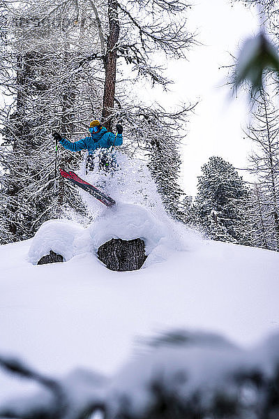 Skifahrer springt im Wald im Schneesturm über einen Baumstumpf