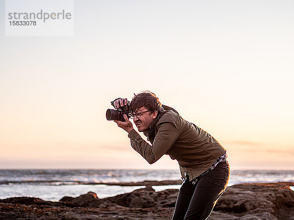 Mann hockt und fotografiert mit Digitalkamera an der Küste