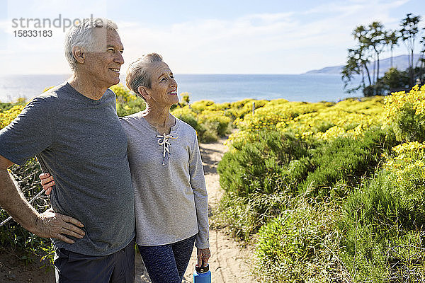 Lächelndes älteres Paar schaut weg  während es an einem sonnigen Tag auf dem Weg gegen den Himmel steht