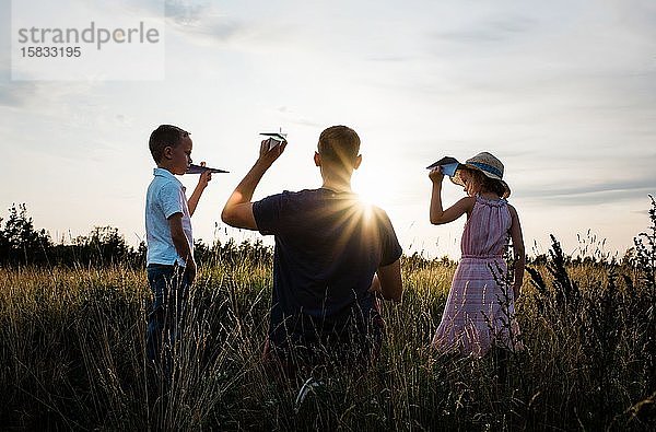 Vater spielt mit seinem Sohn und seiner Tochter bei Sonnenuntergang auf einer Wiese