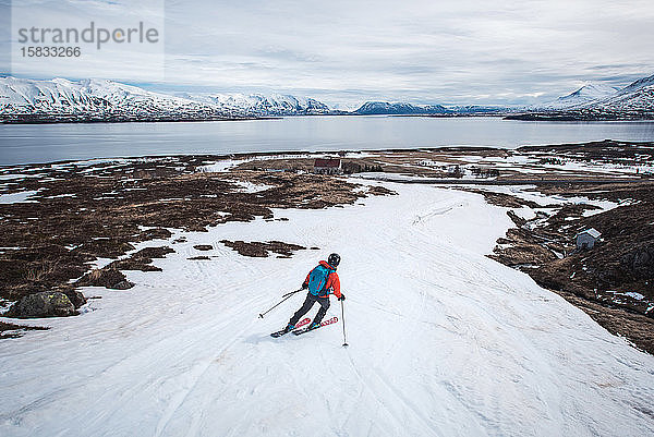 Frau fährt in Island auf Skiern Richtung Meer