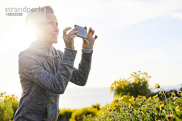 Ältere Frau fotografiert durch ein Smartphone  während sie gegen den Himmel steht