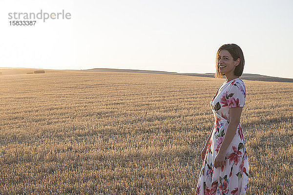 Frau lächelt im Weizenfeld bei Sonnenuntergang