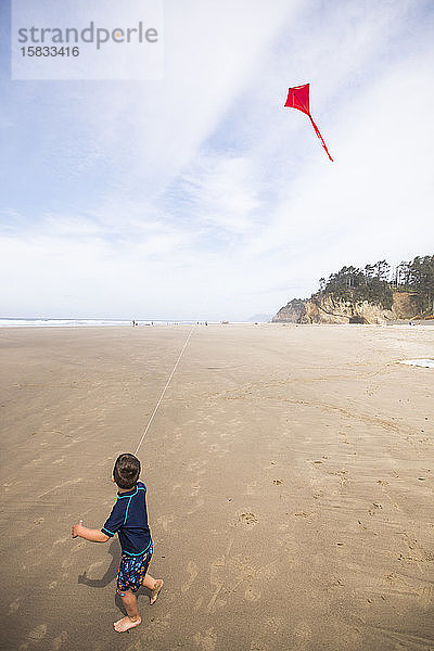 Ein Junge schaut zu einem roten Drachen auf  der am Strand am Himmel fliegt.