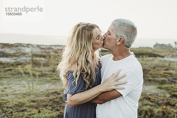 Ehemann und Ehefrau umarmen und küssen sich bei Sonnenuntergang am Strand