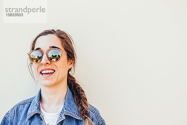 Nahaufnahme einer attraktiven jungen Frau  die mit Sonnenbrille auf pastellfarbenem Hintergrund lacht