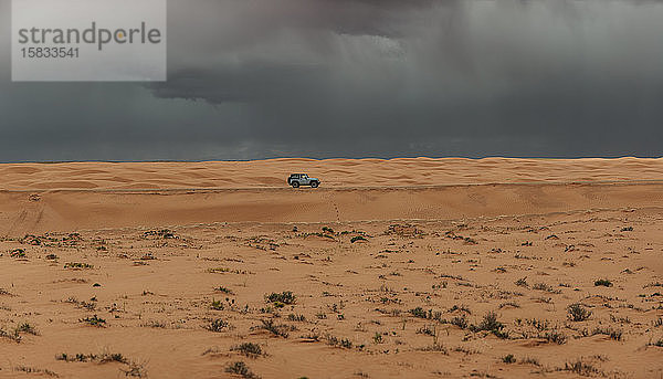 Jeep fährt unter stürmischem Himmel durch die Sanddünen von Utah