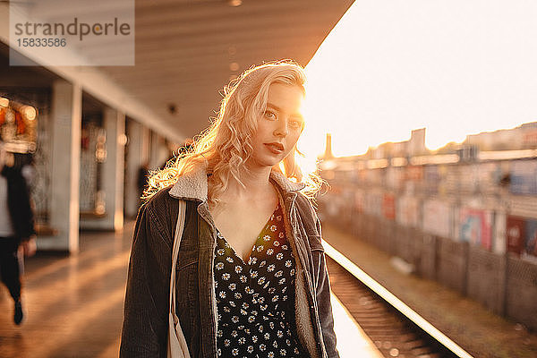 Junge Frau wartet bei Sonnenuntergang am U-Bahnhof auf den Zug