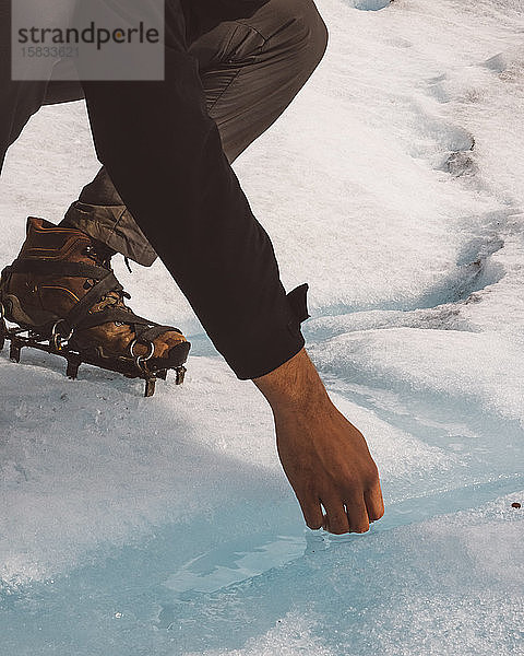 Beine eines Bergsteigers mit Stacheln an den Schuhen  die das Eiswasser berühren