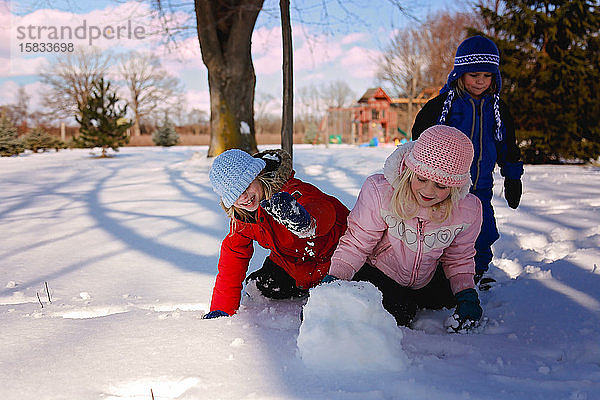 Kinder  die im Winter draußen spielen und einen Schneeball machen
