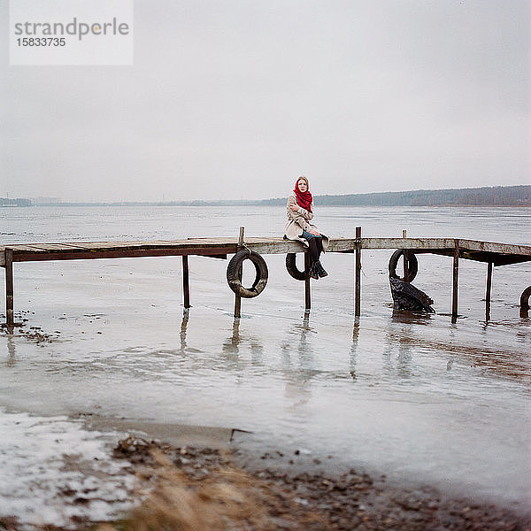 Frau mit rotem Schal am Fluss sitzend