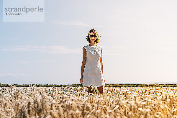 Frau in einem schönen weißen Kleid  die im goldenen Grasfeld steht