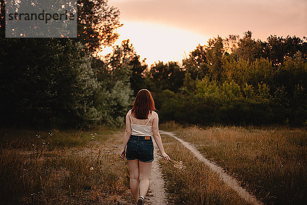 Rückansicht eines Teenager-Mädchens  das im Sommer auf einem Pfad im Wald läuft