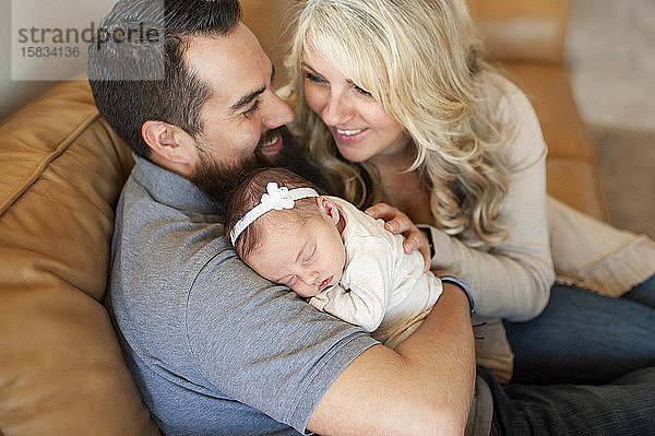 Glücklich lächelnde Familie hält neugeborenes Mädchen zu Hause auf der Couch