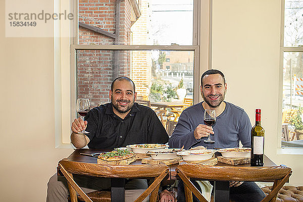 Zwei stolze Geschäftsinhaber sitzen zusammen an einem Restauranttisch mit Wein