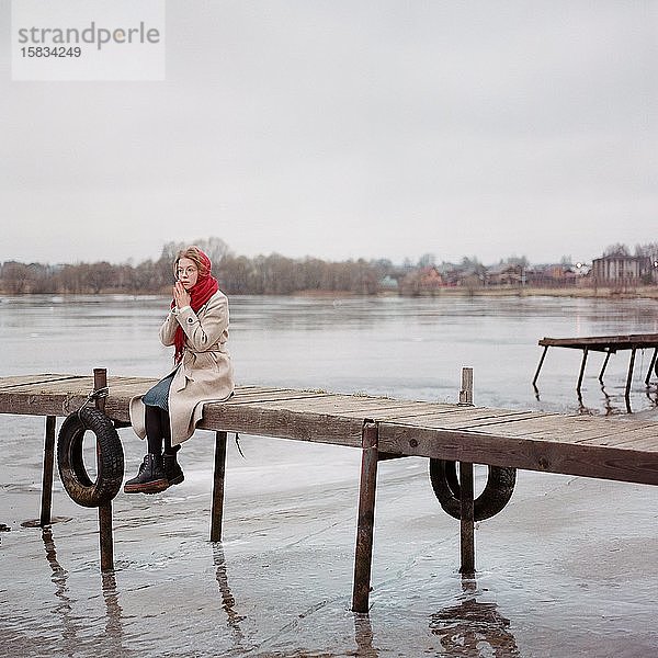 Frau mit rotem Schal am Fluss sitzend